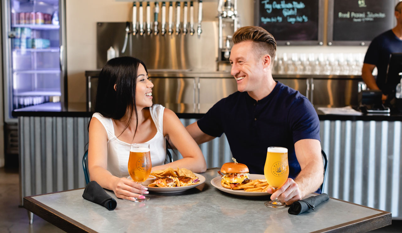 young couple smiling and enjoying a meal and ketch beer in the ketch tasting room