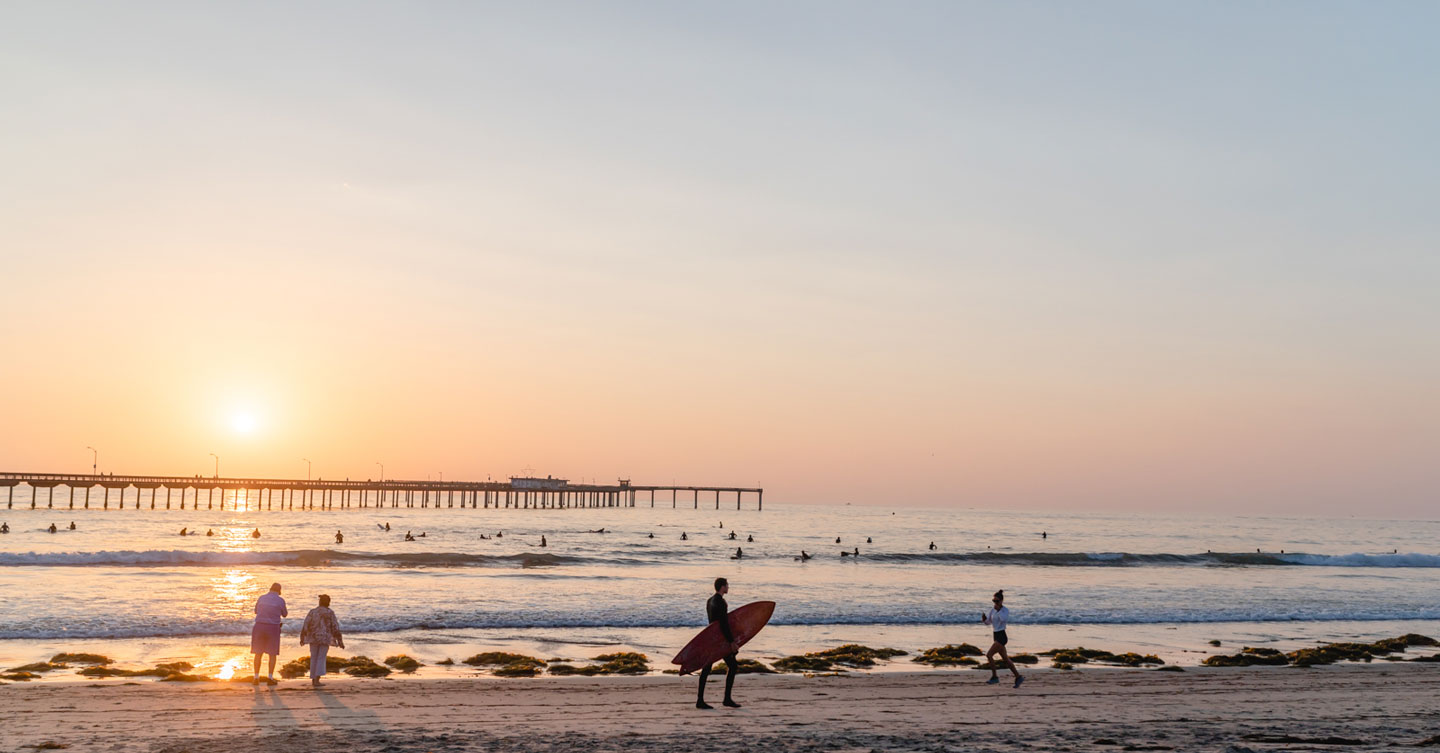 beach with pier in the background during sunset with surfers walking and surfing